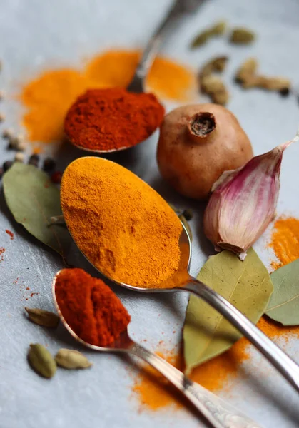 Baharatlı kaşıklar yakın çekim fotoğrafı. Zerdeçal, paprika tozu, bezelye, sarımsak, biber, masada defne yaprağı. Aromatik baharat ve bitkilerin renkli bir resmi. 