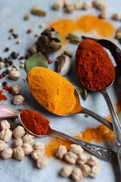 Baharatlı kaşıklar yakın çekim fotoğrafı. Zerdeçal, paprika tozu, bezelye, sarımsak, biber, masada defne yaprağı. Aromatik baharat ve bitkilerin renkli bir resmi. 