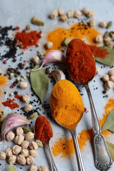 Baharatlı kaşıklar yakın çekim fotoğrafı. Zerdeçal, paprika tozu, bezelye, sarımsak, biber, masada defne yaprağı. Aromatik baharat ve bitkilerin renkli bir resmi. 