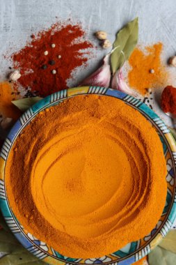 Süslü mavi tabakta zerdeçal tozu var. Aromatik baharatların yakın çekimi. Kırmızı biberli gümüş kaşık. Açık gri arkaplan. Sağlıklı yeme kavramı. 