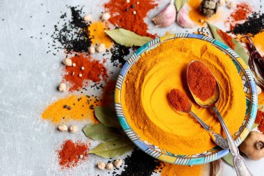 Süslü mavi tabakta zerdeçal tozu var. Aromatik baharatların yakın çekimi. Kırmızı biberli gümüş kaşık. Açık gri arkaplan. Sağlıklı yeme kavramı. 