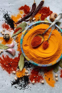 Süslü mavi tabakta zerdeçal tozu var. Aromatik baharatların yakın çekimi. Kırmızı biberli gümüş kaşık. Açık gri arkaplan. Sağlıklı yeme kavramı. 