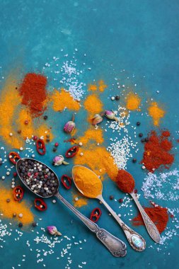 Eski gümüş kaşıklarla dolu bir masa. Aromatik baharatlar ve mavi arka planda bitkiler. Doğal antioksidan konsepti, zerdeçal, kırmızı biber, deniz tuzu, gül rengi.. 