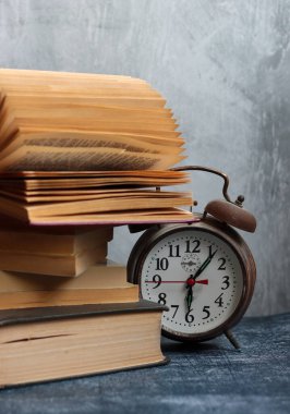 Klasik mekanik çalar saati olan bir hayat. Gri arkaplanda fotokopi alanı olan nesneler. Eski kitap yığınları. Fotoğrafı kapat.. 