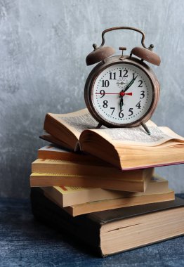 Klasik mekanik çalar saati olan bir hayat. Gri arkaplanda fotokopi alanı olan nesneler. Eski kitap yığınları. Fotoğrafı kapat.. 