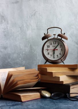 Klasik mekanik çalar saati olan bir hayat. Gri arkaplanda fotokopi alanı olan nesneler. Eski kitap yığınları. Fotoğrafı kapat.. 