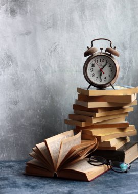 Bir yığın eski kitap, masanın üstünde antika bir saat. Açık gri desenli arkaplan ve kopyalama alanı. Eğitim kavramı. 