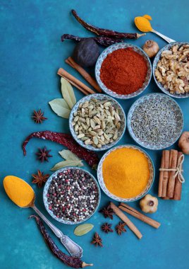 Mavi seramik kaselerdeki baharat ve bitkilerin fotoğrafını çek. Paprika, zerdeçal, anason, lavanta, kakule, tarçın, biber dokulu mavi arka plan. 