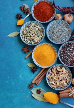 Mavi seramik kaselerdeki baharat ve bitkilerin fotoğrafını çek. Paprika, zerdeçal, anason, lavanta, kakule, tarçın, biber dokulu mavi arka plan. 