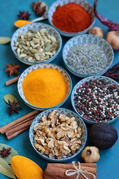 Close up photo of spices and herbs in blue ceramic bowls. Paprika, turmeric, anise, lavender, cardamom, cinnamon, pepper on textured blue background.
