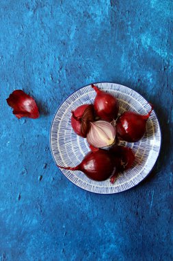 Mavi tabakta kırmızı soğan. Taze sebzelerin fotoğrafını çek. Fotokopi alanı olan dokulu mavi arka planda soğanlı bir hayat. Sağlıklı yeme kavramı. 