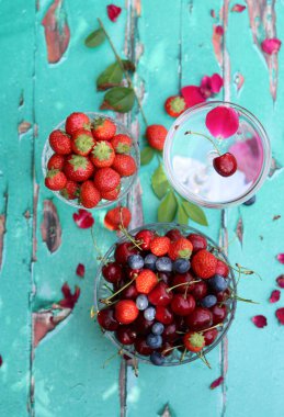 Eski ahşap masada taze yaz meyveleriyle dolu cam kaseler. Bahçede kahvaltı var. Yabanmersini, çilek, tatlı kiraz yakın plan fotoğraf. 