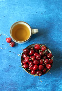 Masada bitki çayı ve bir kase kiraz. Basit kompozisyon hala yaz meyveleriyle dolu.. 
