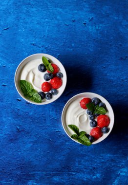 Taze böğürtlenli iki yoğurt kasesi. Sağlıklı kahvaltı manzaralı fotoğraf. Kopya alanı olan mavi desenli arkaplan. Güzel yaz sakin hayat. Sağlıklı yeme kavramı. 