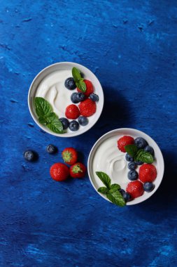 Taze böğürtlenli iki yoğurt kasesi. Sağlıklı kahvaltı manzaralı fotoğraf. Kopya alanı olan mavi desenli arkaplan. Güzel yaz sakin hayat. Sağlıklı yeme kavramı. 