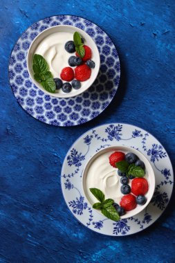 Taze böğürtlenli iki yoğurt kasesi. Sağlıklı kahvaltı manzaralı fotoğraf. Kopya alanı olan mavi desenli arkaplan. Güzel yaz sakin hayat. Sağlıklı yeme kavramı. 