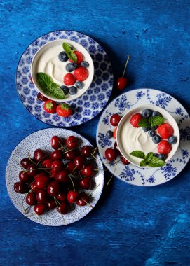 Organik çilek, yabanmersini, kiraz ve nane yapraklı sütsüz yoğurt. Masada sağlıklı vejetaryen kahvaltısı. Taze yaz meyvelerinin en iyi görüntüsü. 