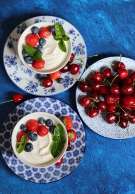 Organik çilek, yabanmersini, kiraz ve nane yapraklı sütsüz yoğurt. Masada sağlıklı vejetaryen kahvaltısı. Taze yaz meyvelerinin en iyi görüntüsü. 