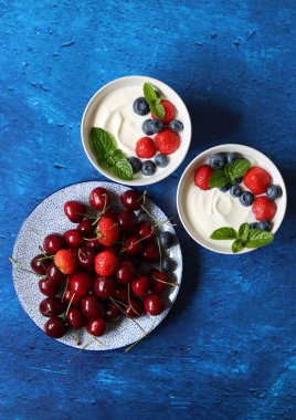 Organik çilek, yabanmersini, kiraz ve nane yapraklı sütsüz yoğurt. Masada sağlıklı vejetaryen kahvaltısı. Taze yaz meyvelerinin en iyi görüntüsü. 
