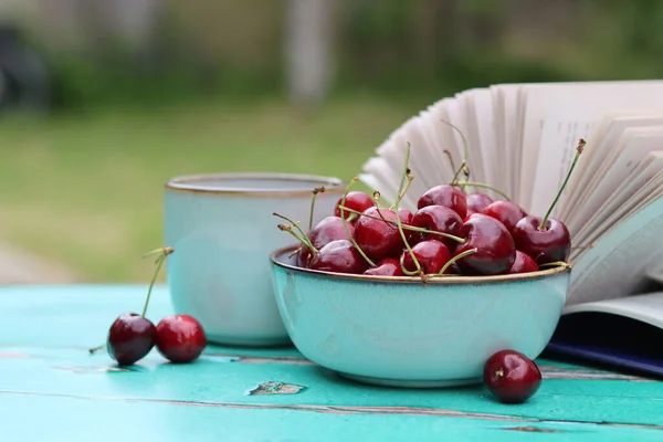 Süßkirschschale Becher Kräutertee Und Ein Aufgeschlagenes Buch Auf Einem Grünen — Stockfoto