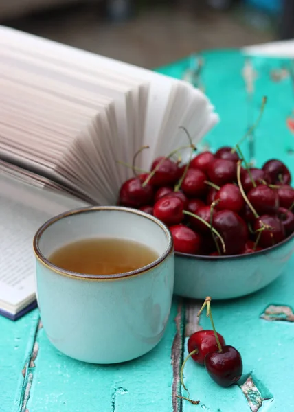 Süßkirschschale Becher Kräutertee Und Ein Aufgeschlagenes Buch Auf Einem Grünen — Stockfoto