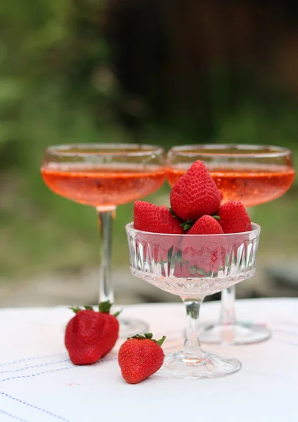 Spritz cocktails and fresh strawberry in a glass bowl. Picnic in the garden. Glass tableware close up photo. Rustic still life with seasonal fruit.
