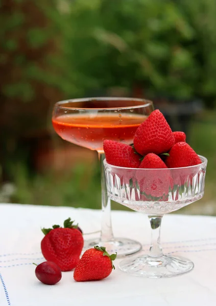 Glass with cocktail and fresh strawberry on a garden table. Green tree leaves on a background. Summer day evening.