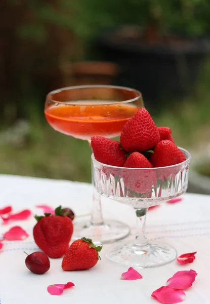 Glass with cocktail and fresh strawberry on a garden table. Green tree leaves on a background. Summer day evening.