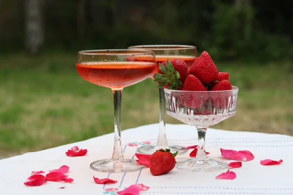 Spritz cocktails and fresh strawberry in a glass bowl. Picnic in the garden. Glass tableware close up photo. Rustic still life with seasonal fruit.