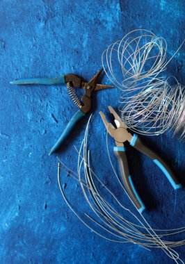 Close up photo of pliers and aluminum wire on blue textured background. Industrial still life with handyman tools.  