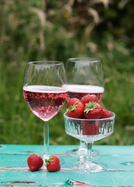 Masada iki bardak köpüklü gül şarabı ve çilek. Açık havada romantik bir piknik. Cam sofra takımının fotoğrafını kapat. Yaz içecekleri ve yiyecekler. 