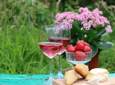 Bahçede güneşli bir gün. Taze meyve, çiçekler, peynir ve şarap. Arka planda yeşil çimenler. Metin için boş boşluk. 