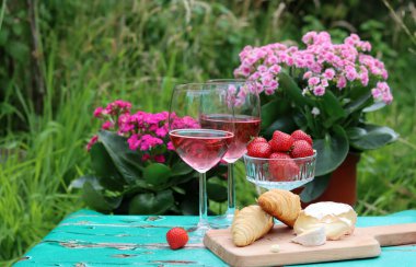 Bahçede güneşli bir gün. Taze meyve, çiçekler, peynir ve şarap. Arka planda yeşil çimenler. Metin için boş boşluk. 