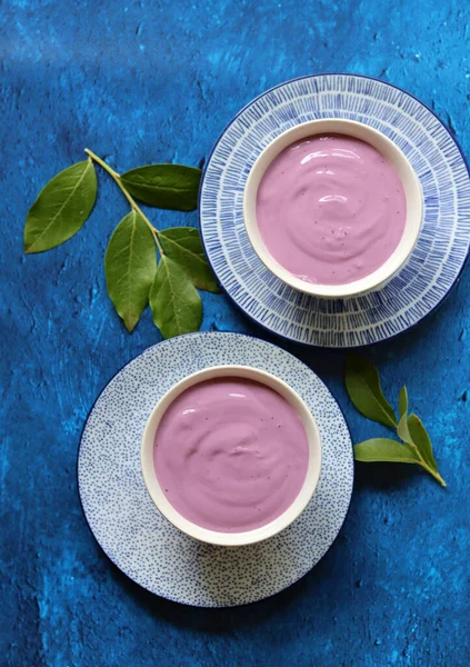 Greek yogurt in a bowl, blueberry leaves on textured background with copy space. Healthy non-dairy yogurt with blueberry. Food still life photo.