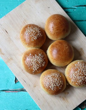 Home baked buns with sesame seeds on wooden board. Close up photo of crusty sourdough buns. 