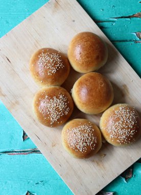 Home baked buns with sesame seeds on wooden board. Close up photo of crusty sourdough buns. 