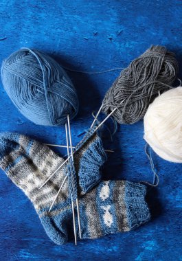Balls of yarn, knitted socks with colorful pattern. Hand made sock close up photo. Wool yarn, knitting needles on blue textured background with copy space. 