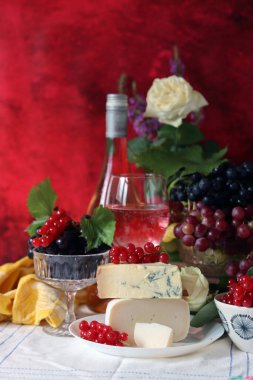 Wine, cheese, fruit and flowers on a table. Vibrant colors of fresh berries and grapes. Colorful still life with glass of pink wine, red and white grapes, gorgonzola cheese and red currant. 