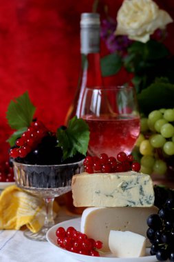 Wine, cheese, fruit and flowers on a table. Vibrant colors of fresh berries and grapes. Colorful still life with glass of pink wine, red and white grapes, gorgonzola cheese and red currant. 