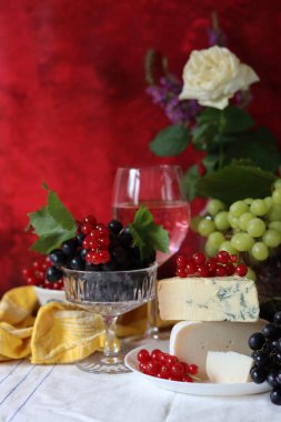 Camembert cheese, green and black grapes, glass of rose wine on a table. Colorful summer still life with seasonal fruit and berries. 