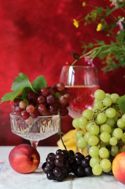 Glass of pink wine, grapes, berries and flowers on a table. Delicious summer food close up photo. Textured background with copy space.