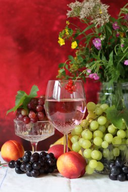 Wine, cheese, fruit and flowers on a table. Vibrant colors of fresh berries and grapes. Colorful still life with glass of pink wine, red and white grapes, gorgonzola cheese and red currant. 