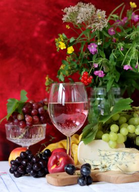 Wine, cheese, fruit and flowers on a table. Vibrant colors of fresh berries and grapes. Colorful still life with glass of pink wine, red and white grapes, gorgonzola cheese and red currant. 