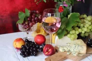 Camembert cheese, green and black grapes, glass of rose wine on a table. Colorful summer still life with seasonal fruit and berries. 