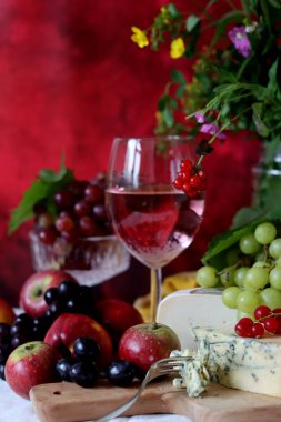 Camembert cheese, green and black grapes, glass of rose wine on a table. Colorful summer still life with seasonal fruit and berries. 