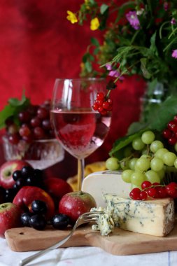 Camembert cheese, green and black grapes, glass of rose wine on a table. Colorful summer still life with seasonal fruit and berries. 
