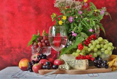 Glass of pink wine, grapes, berries and flowers on a table. Delicious summer food close up photo. Textured background with copy space.