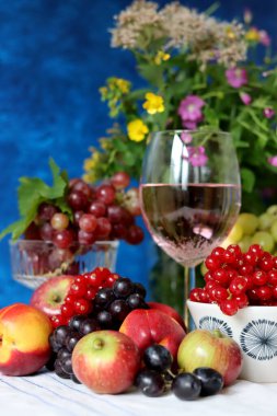 Glass of pink wine, grapes, berries and flowers on a table. Delicious summer food close up photo. Textured background with copy space.