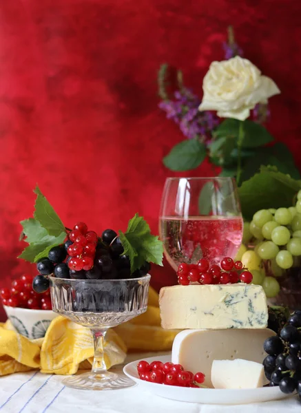 Camembert cheese, green and black grapes, glass of rose wine on a table. Colorful summer still life with seasonal fruit and berries. 