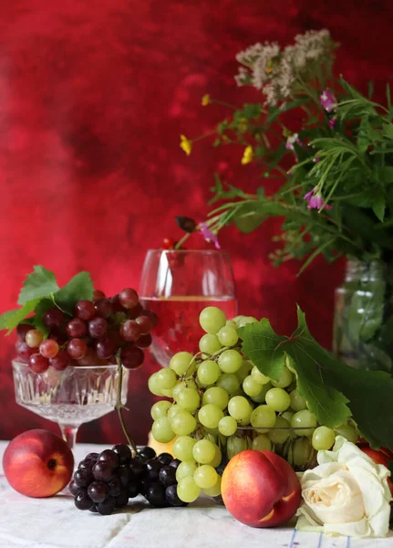 Glass of pink wine, grapes, berries and flowers on a table. Delicious summer food close up photo. Textured background with copy space.